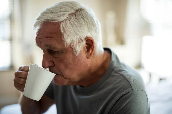 Беспокойный пожилой человек пьет черный кофе в спальне — стоковое фото