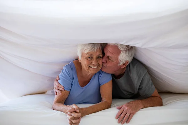 Senior man kysser kvinna under filt på säng — Stockfoto