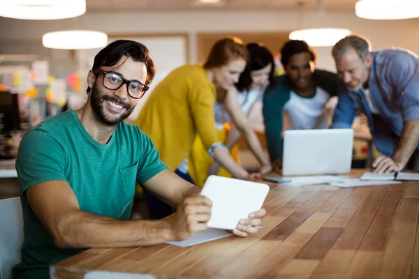 Mann nutzt digitales Tablet, während Team im Hintergrund arbeitet — Stockfoto