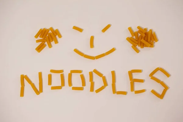 Smiley face and noodles text made out of pennette pasta — Stock Photo, Image