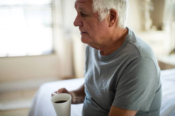 Задумчивый старший мужчина держит кружку черного кофе в спальне — стоковое фото