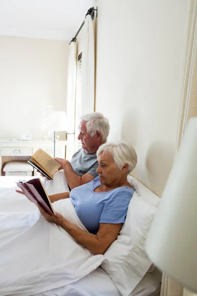 Старшая пара читает книги в спальне — стоковое фото