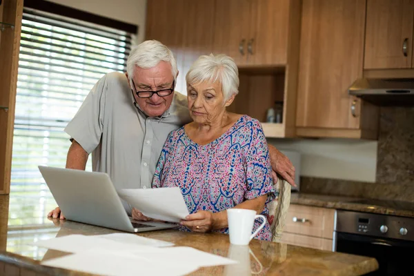 Senior couple calculating their invoices with laptop in the kitchen — Stock Photo, Image