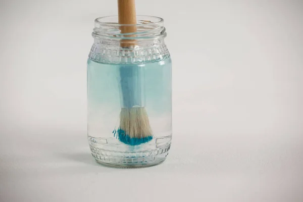 Pincel con pintura azul sumergido en un frasco lleno de agua — Foto de Stock