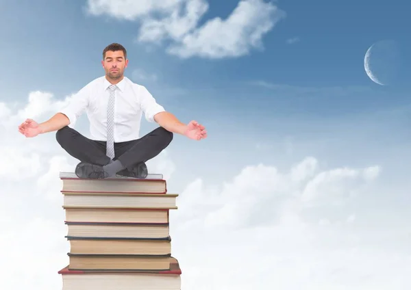 Businessman meditating sitting on Books stacked by blue sky — Stock Photo, Image