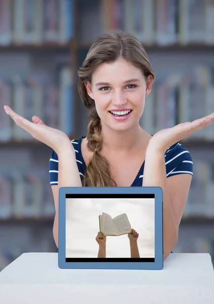 Kvinnan vid bordet med tablett visar händer med boken mot suddiga bokhylla med blå overlay — Stockfoto