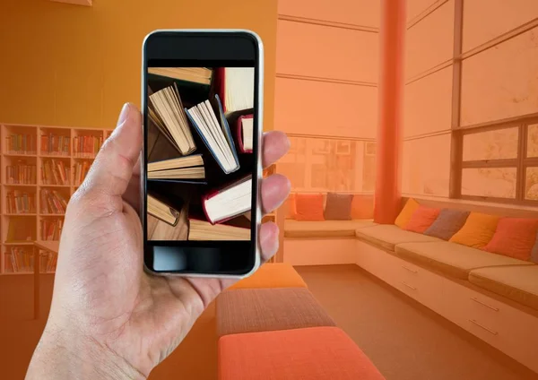 Mão com telefone mostrando livros de pé contra quarto com sobreposição de laranja — Fotografia de Stock