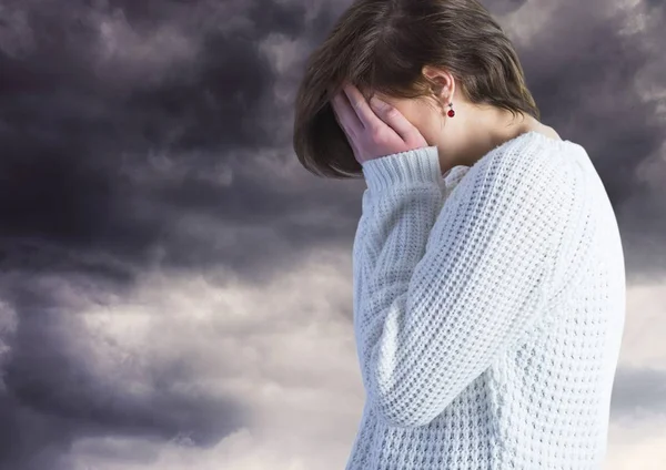 Sad woman with face in hands against dark clouds — Stock Photo, Image