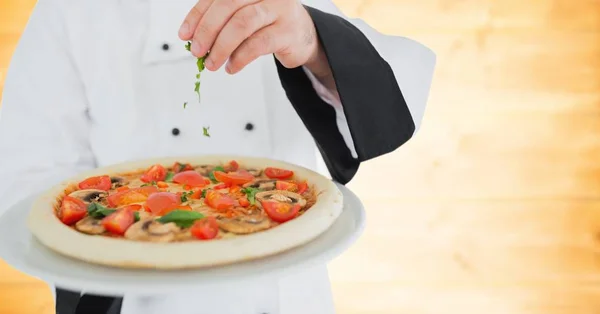 Szef kuchni, zakładanie zioła pizza przeciwko rozmyte żółty panel drewna — Zdjęcie stockowe