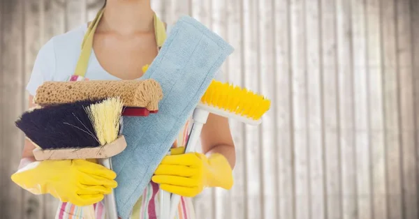 Femme en tablier avec brosses contre panneau de bois flou — Photo