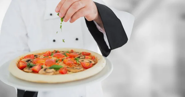Szef kuchni, zakładanie pizza przeciwko rozmyte tło szare zioła — Zdjęcie stockowe