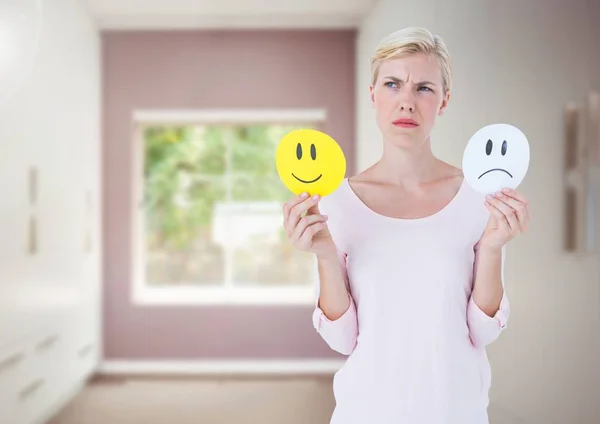 Women holding faces deciding happy or sad emotions against room — Stock Photo, Image