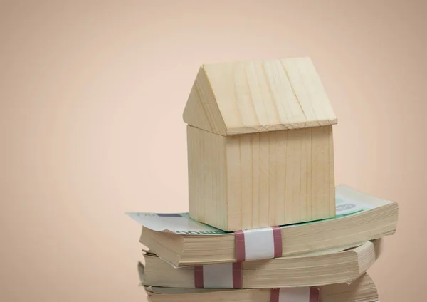 Casa de madera sentada sobre billetes de pila de dinero sobre fondo beige — Foto de Stock