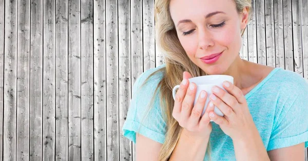 Nahaufnahme einer Frau, die auf eine weiße Tasse gegen eine graue Holzplatte blickt — Stockfoto