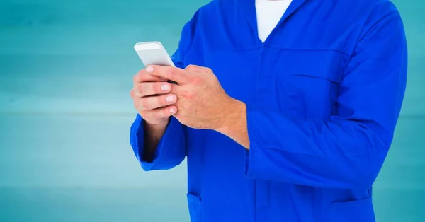 Mechanic holding up phone against blurry blue wood panel — Stock Photo, Image
