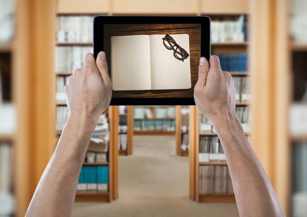 Hands with tablet showing open book and glasses against blurry archways — Stock Photo, Image