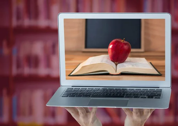 Hands with laptop showing book with red apple against blurry bookshelf with red overlay — Stock Photo, Image