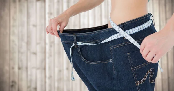 Kadın büyük pantolon ve bulanık ahşap panel karşı ölçüm bandı ile — Stok fotoğraf