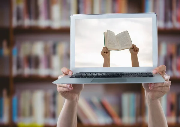 Hands with laptop showing hands with book against blurry bookshelf — Stock Photo, Image