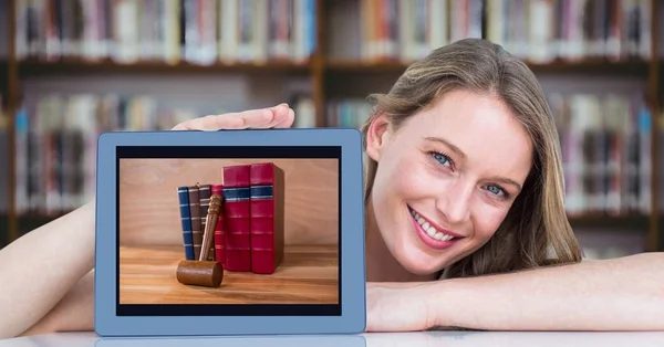 快乐的妇女坐在图书馆的桌子上堆书介绍平板电脑 — 图库照片