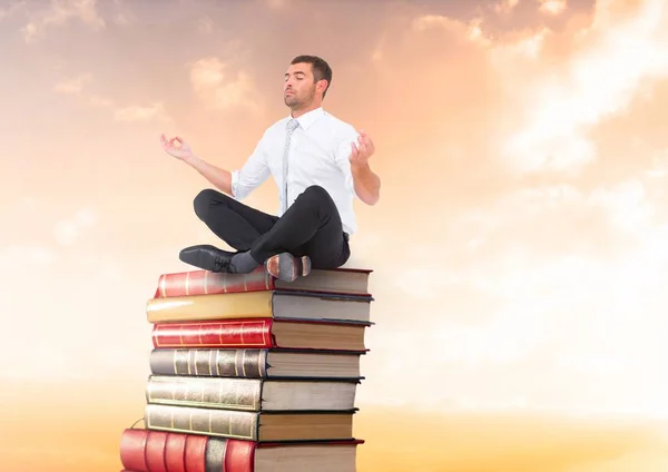 Empresário meditando sentado em livros empilhados pelo pôr do sol com laptop — Fotografia de Stock