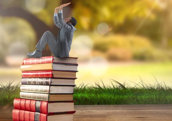 Uomo d'affari seduto su libri accatastati dal verde natura — Foto Stock