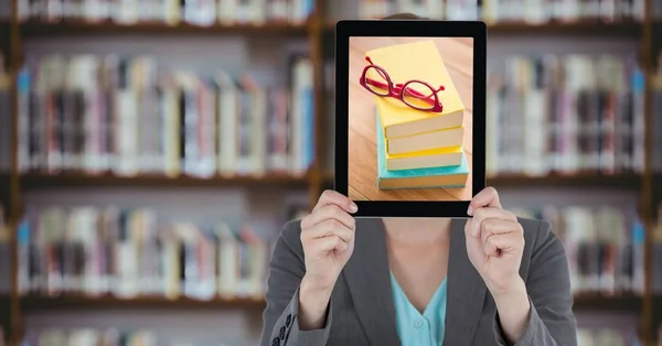 Femme d'affaires avec tablette sur son visage avec des piles de livres tout en se tenant à la bibliothèque — Photo