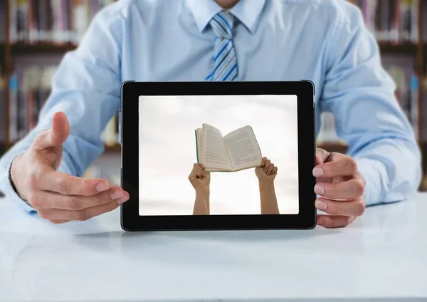 Homme d'affaires à table avec tablette montrant les mains avec livre contre bibliothèque floue — Photo