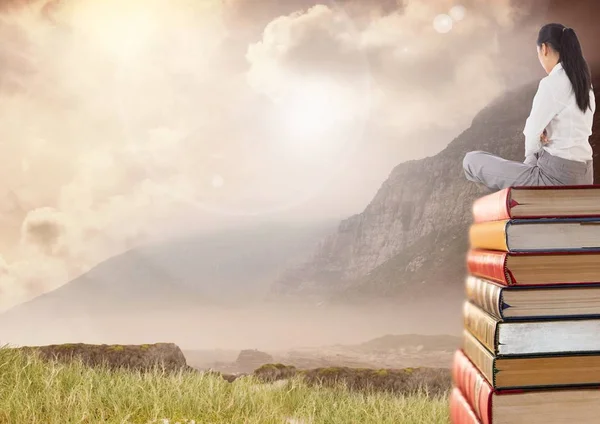 Mujer sentada en libros apilados por el cielo de montaña —  Fotos de Stock