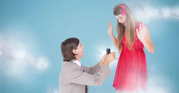 Man proposing to woman against blue background with clouds — Stock Photo, Image