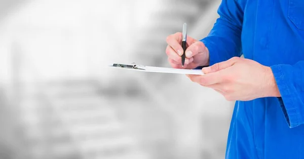 Mechanic with clipboard against blurry grey stairs — Stock Photo, Image