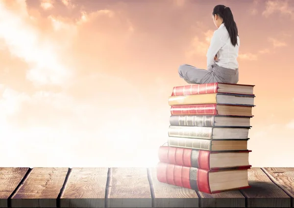 Zakenvrouw zittend op boeken gestapeld door zonnige wolken — Stockfoto