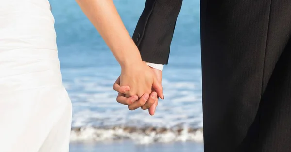 Sposa e sposo corpi inferiori tenendosi per mano contro spiaggia sfocata riva — Foto Stock