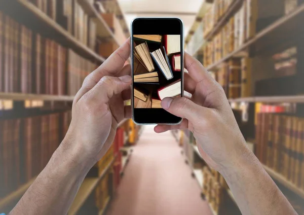Hand mit Telefon zeigt stehende Bücher gegen verschwommene Bücherregale — Stockfoto