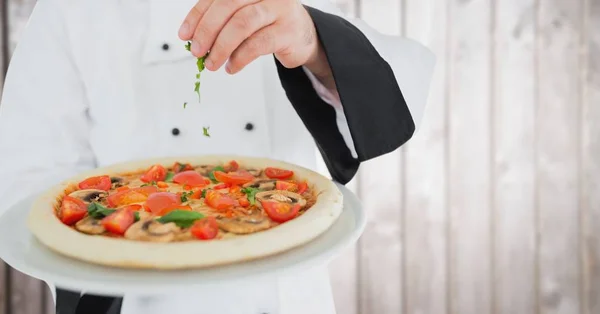 Koch setzt Kräuter auf Pizza gegen verschwommene Holzplatte — Stockfoto