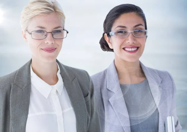 Two business women with flare against blurry grey wood panel — Stock Photo, Image