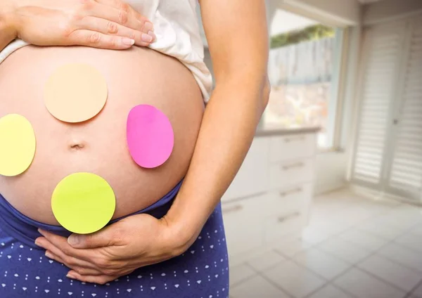 Έγκυος γυναίκα ενότητα με αυτοκόλλητες σημειώσεις στο στομάχι σε θολές κουζίνα μέσα — Φωτογραφία Αρχείου