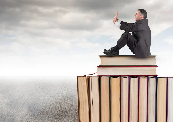 Hombre sentado en libros apilados por un cielo gris nublado —  Fotos de Stock