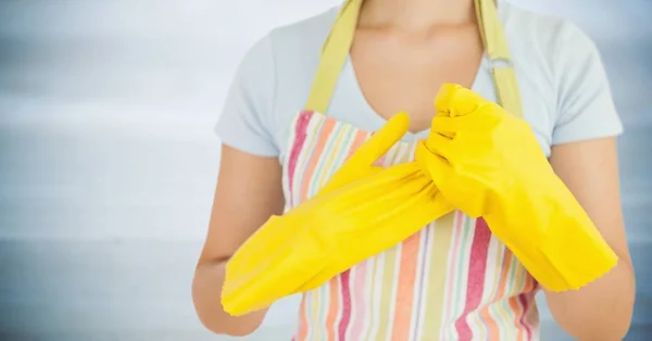 Mujer en delantal con guantes amarillos contra panel de madera gris borroso — Foto de Stock