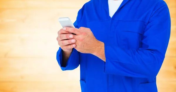 Mechanic holding up phone against blurry yellow wood panel — Stock Photo, Image