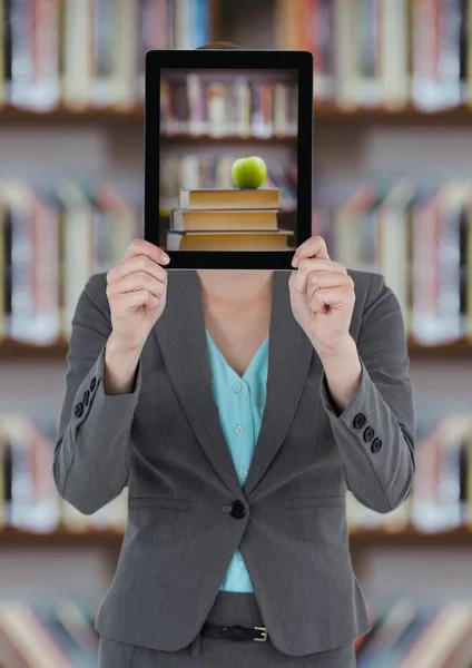 Business woman with tablet showing book pile with green apple against blurry bookshelf — Stock Photo, Image