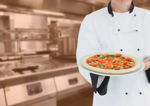 Chef-kok met pizza tegen wazig keuken met oranje overlay — Stockfoto