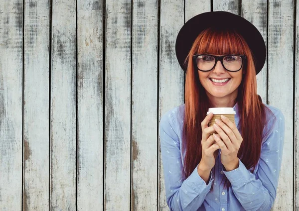 Kvinna i hatt med kaffekopp mot träpanel — Stockfoto