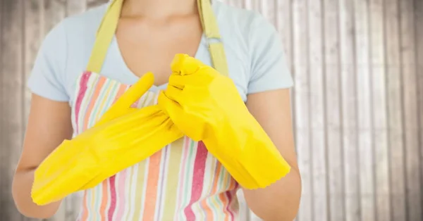 Frau in Schürze mit Handschuhen gegen verschwommene Holzplatte — Stockfoto