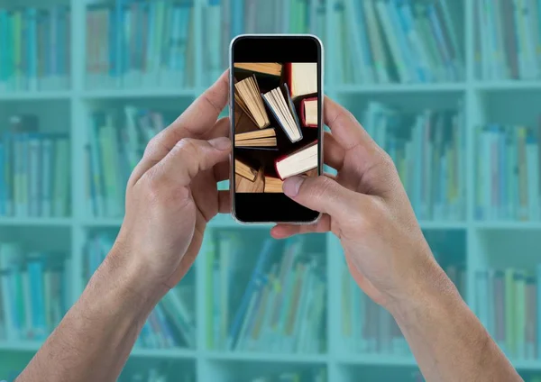 Τα χέρια με το τηλέφωνο δείχνει βιβλία στέκεται ενάντια θολή ράφι με επικάλυψη κιρκίρι — Φωτογραφία Αρχείου