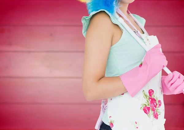 Woman in apron with duster against blurry pink wood panel — Stock Photo, Image