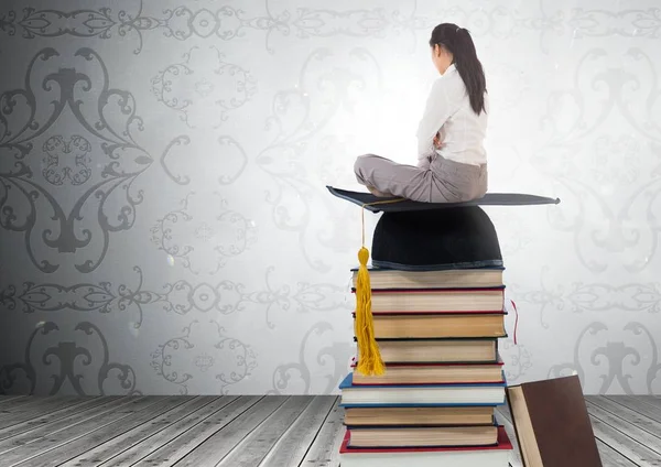 Vrouw zitten op boeken gestapeld door decoratieve behang met afstuderen hoed — Stockfoto