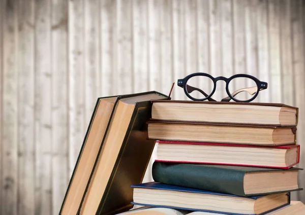 Pile de livres et de verres contre panneau de bois flou — Photo