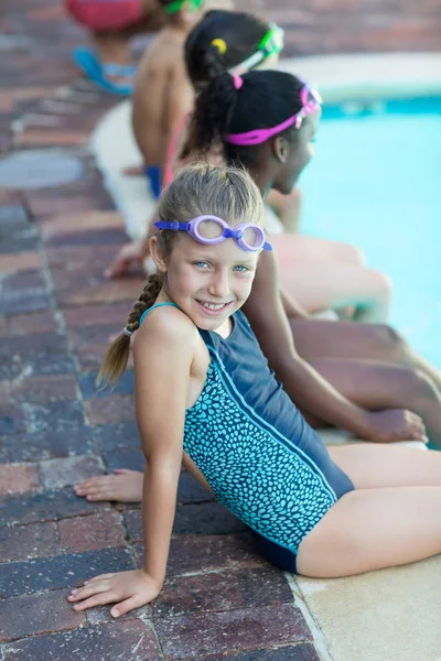 Menina bonito sentado com amigos na beira da piscina — Fotografia de Stock