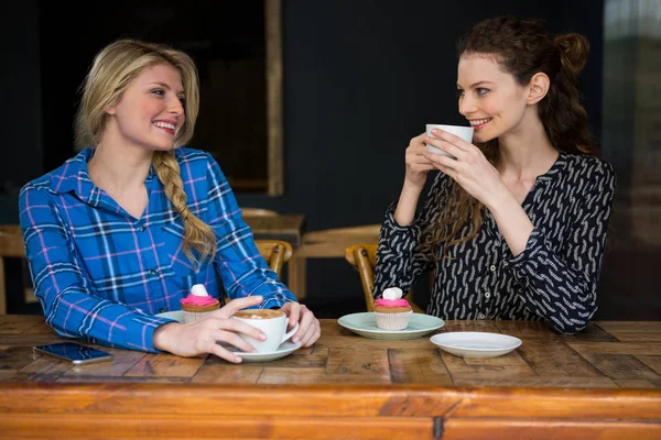 Amigos do sexo feminino tomar café enquanto conversa na cafetaria — Fotografia de Stock